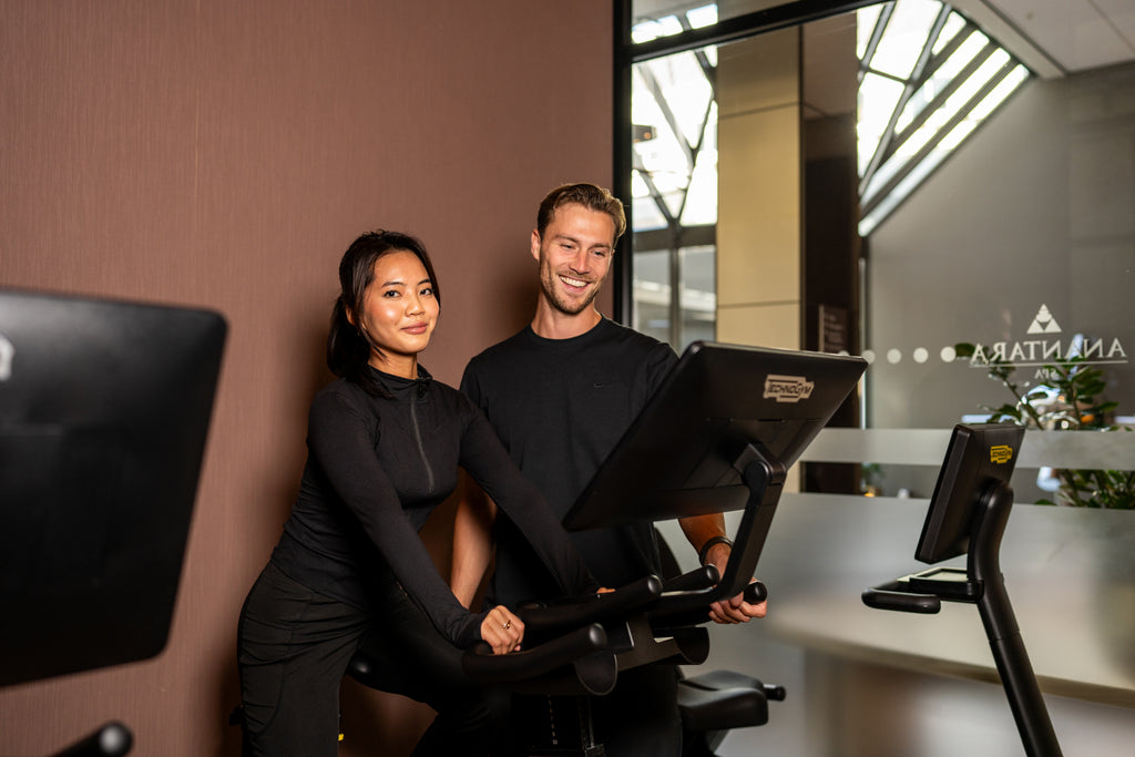 Vrouw op een hometrainer terwijl de trainer achter haar de instellingen op het scherm aanwijst