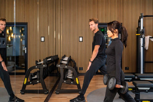 Vrouw zakt door in een split squat met dumbbells terwijl de trainer geknield de uitvoering beoordeelt